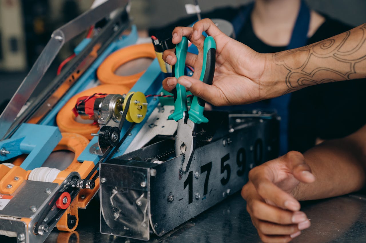 Close-up of hands using pliers on machinery, showcasing technical repair work.